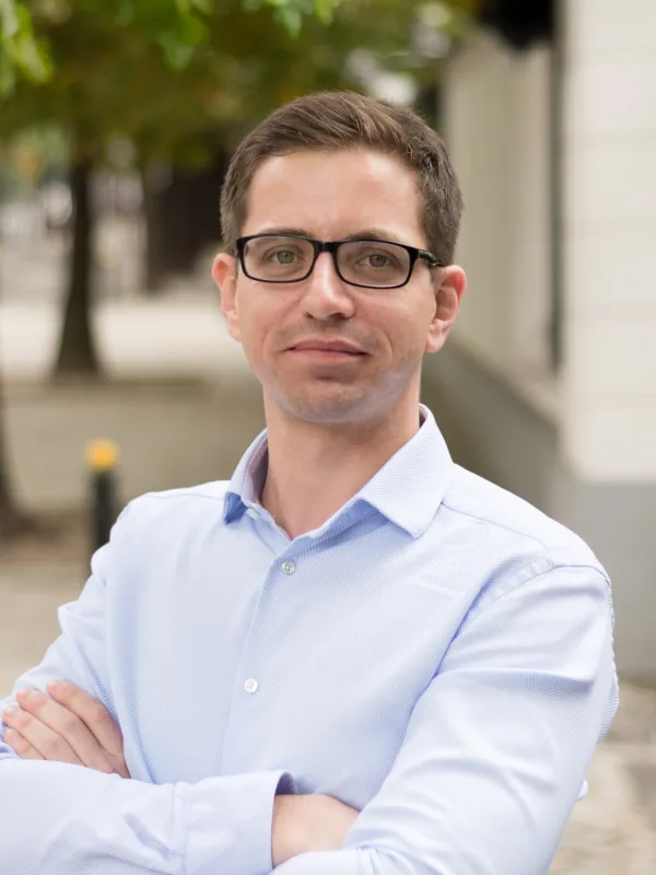 Kamil Feret looking towards the camera wearing a light blue shirt against a blurred background of a street