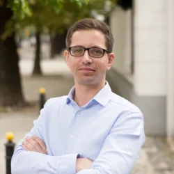 Kamil Feret looking towards the camera wearing a light blue shirt against a blurred background of a street