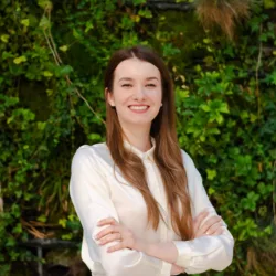 Małgorzata arms folded smiling to camera in front of a green hedge