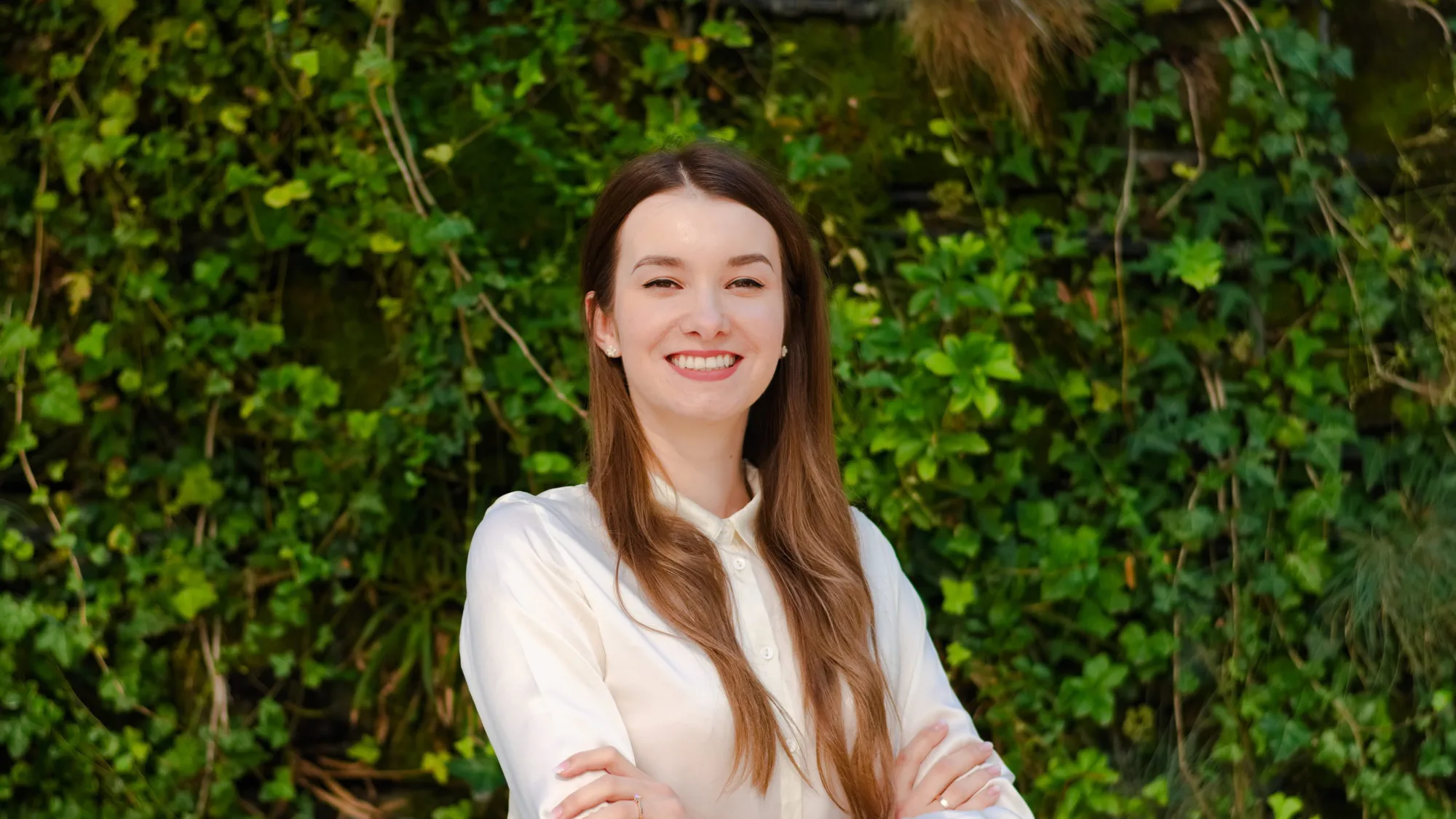 Małgorzata arms folded smiling to camera in front of a green hedge