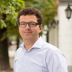 Wojtek Stec in pale blue shirt with street background of trees and white walls