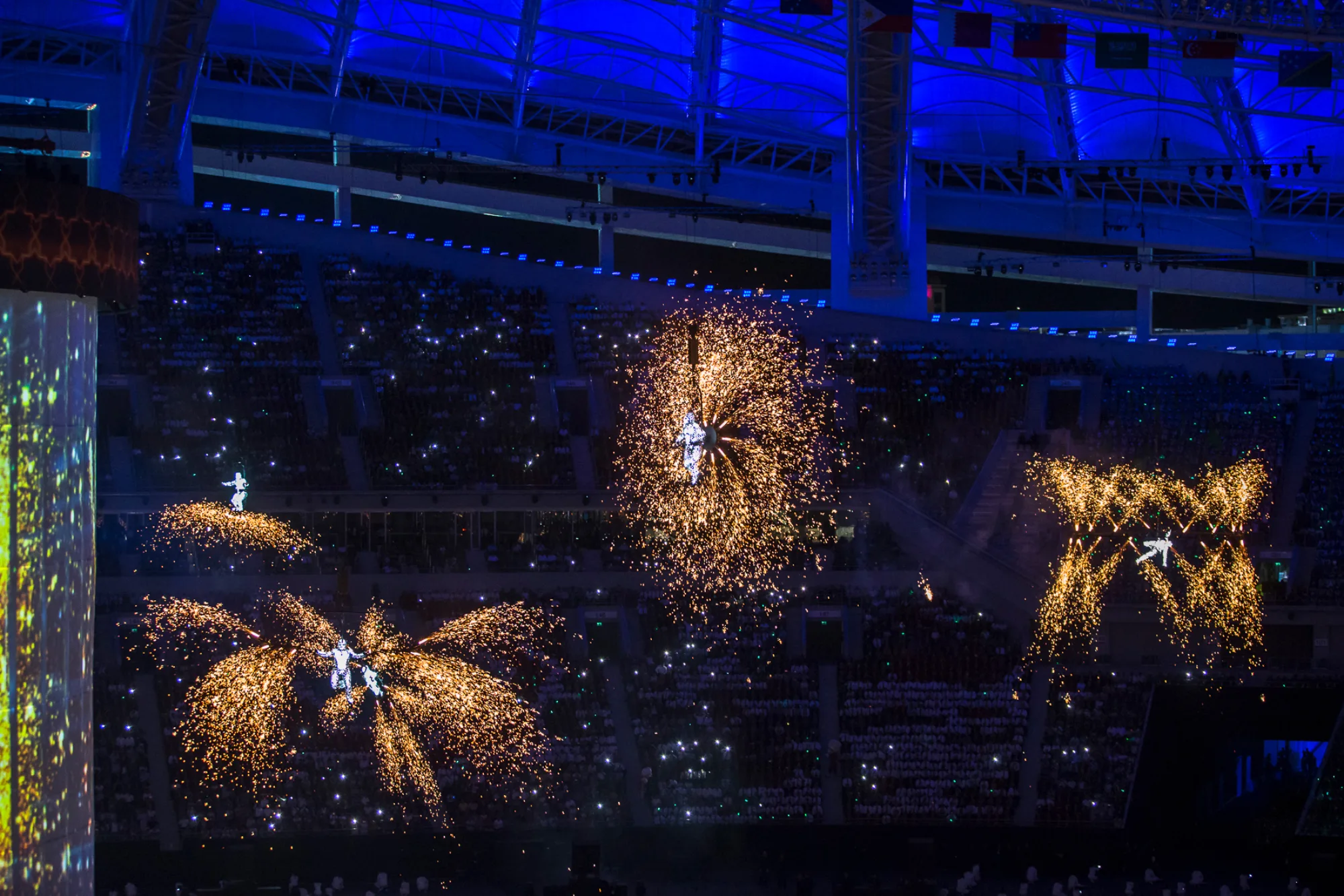 Four flying performers surrounded by pyrotechnics in a dark arena