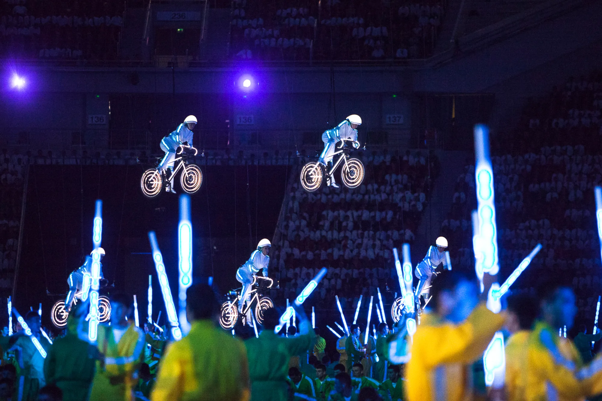 Illuminated cyclists with neon lights on their clothing and bikes suspended on wires