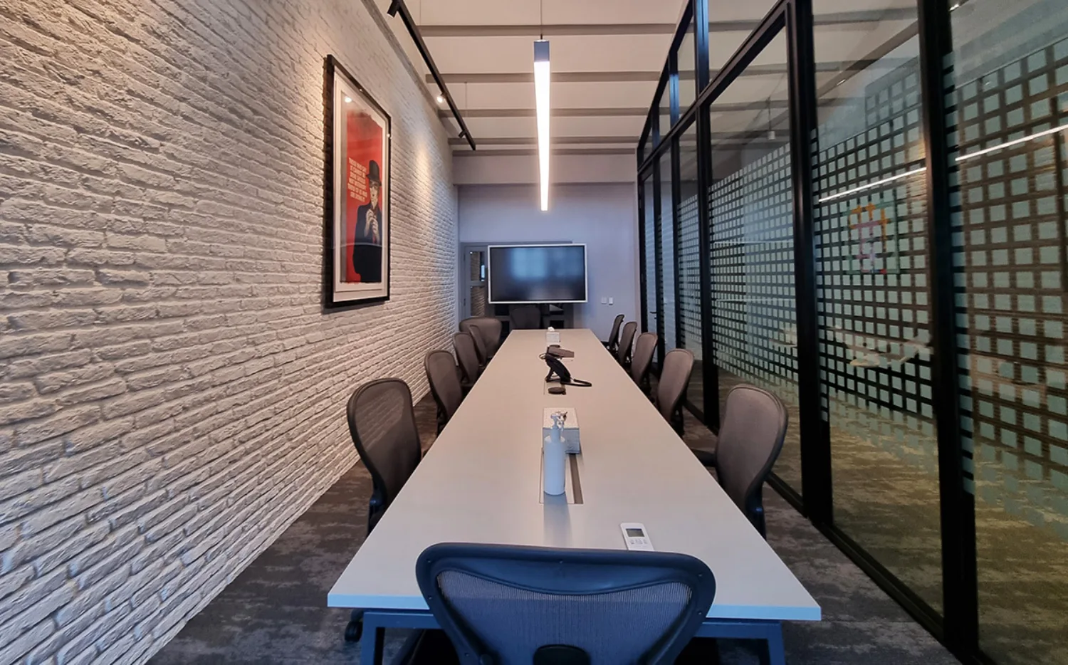 Meeting room office room with long table and seating with glass and brick walls and soft lighting.