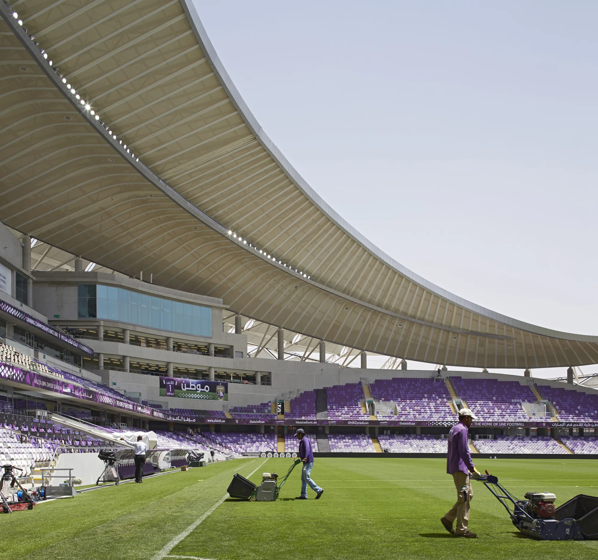 Internal shot of the pitch with men mowing grass and seating in background