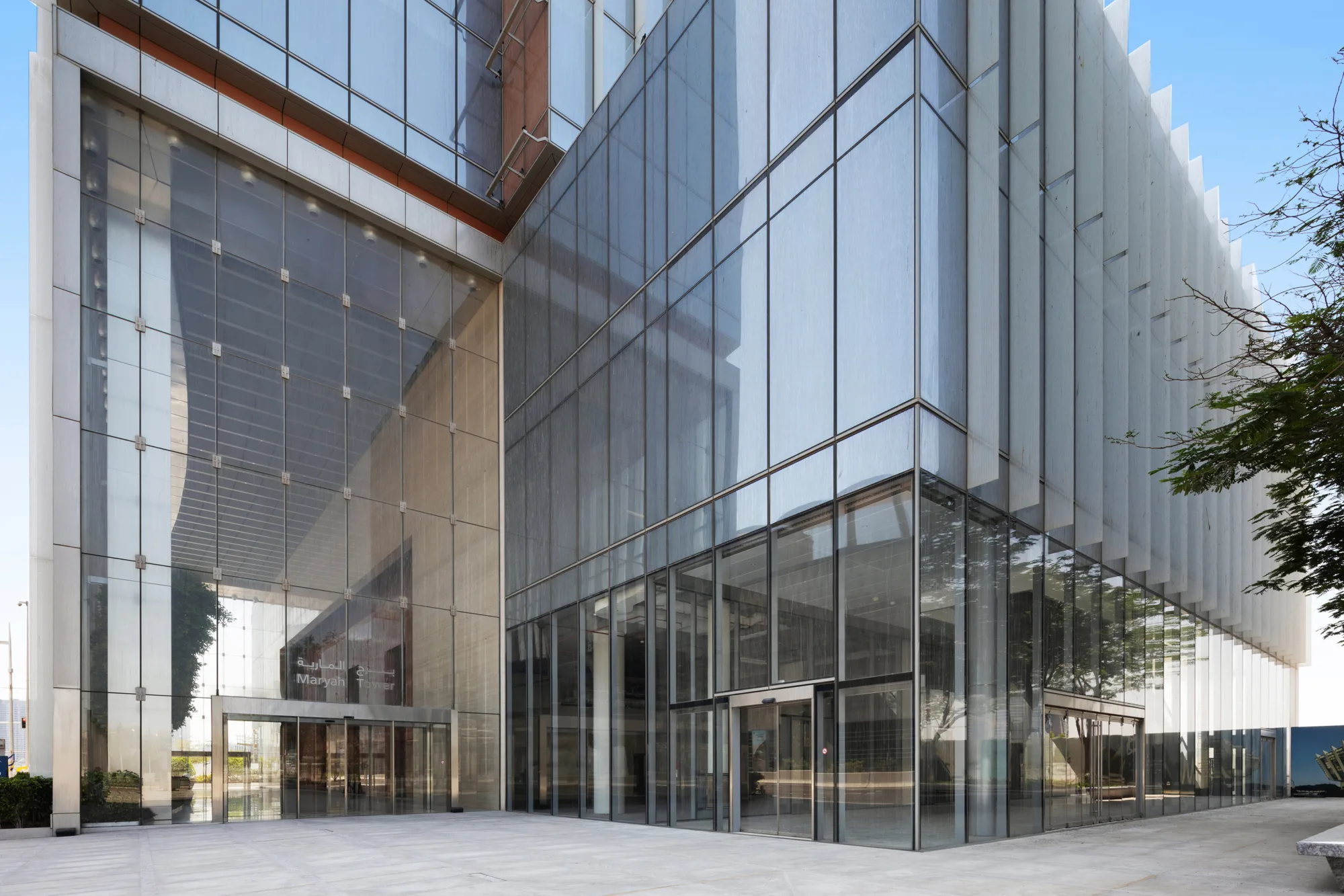 Entrance of a high-rise building with glass walls and architectural detailing; includes surrounding pavement and greenery.