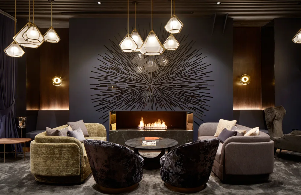 Velvet chairs in front of a central fireplace in a dark walled plush lounge