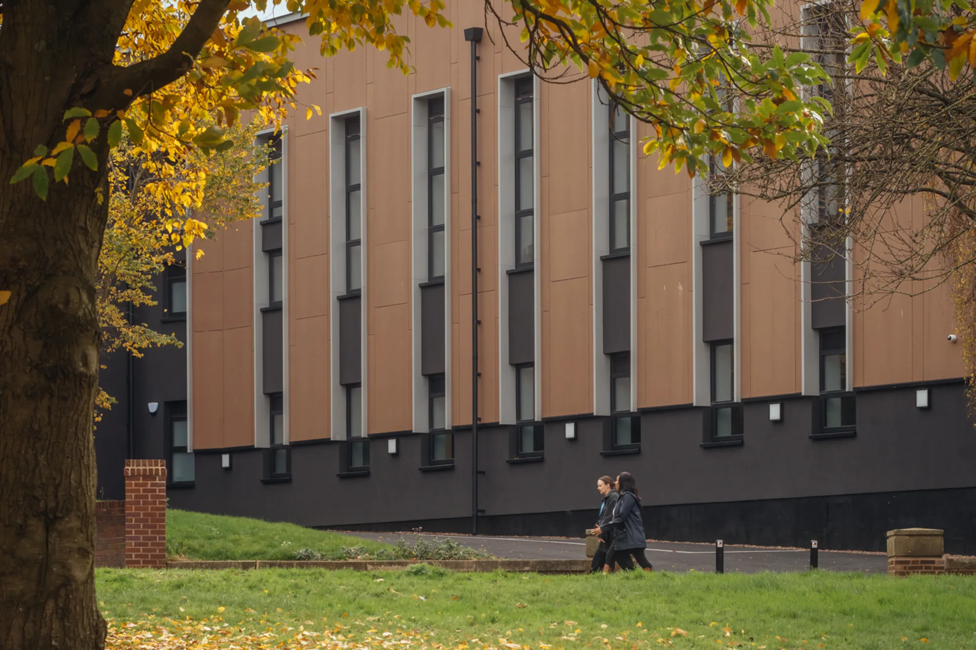 Side view of the Animal Studies Centre from a nearby park with people walking across in the distance.