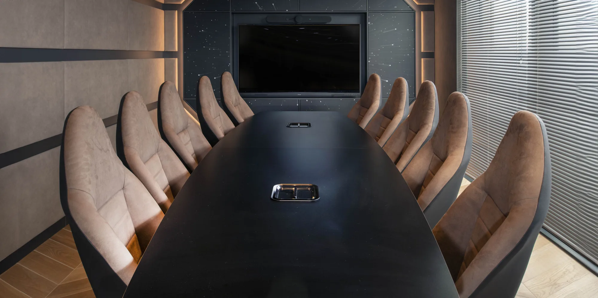 Symmetrical image of an office meeting room, with a long modern black table with 5 modern chairs either side and a tv on the back wall