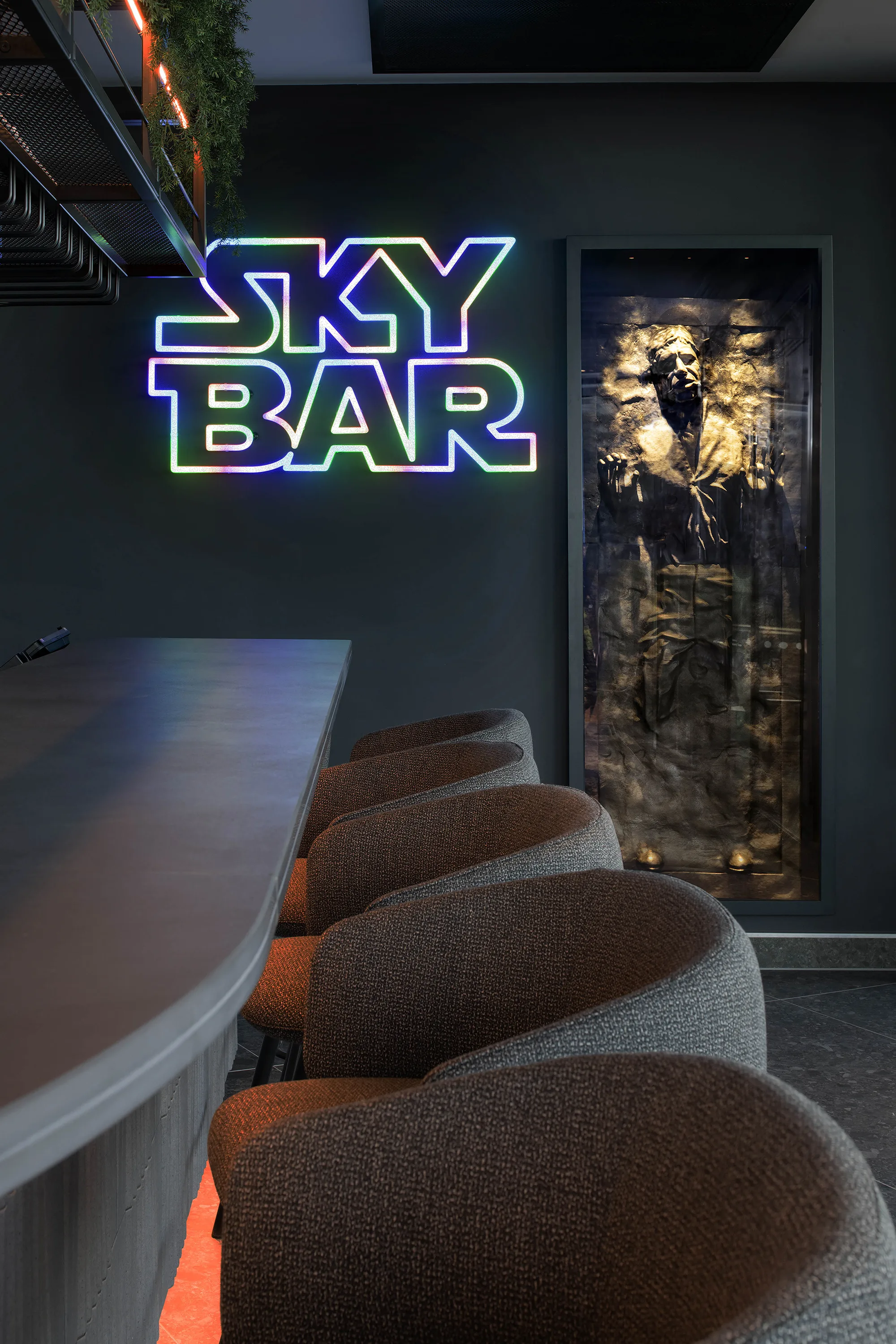Image of the sky bar, a dark and moody bar with 4 stools and a neon sign in star wars font saying sky bar