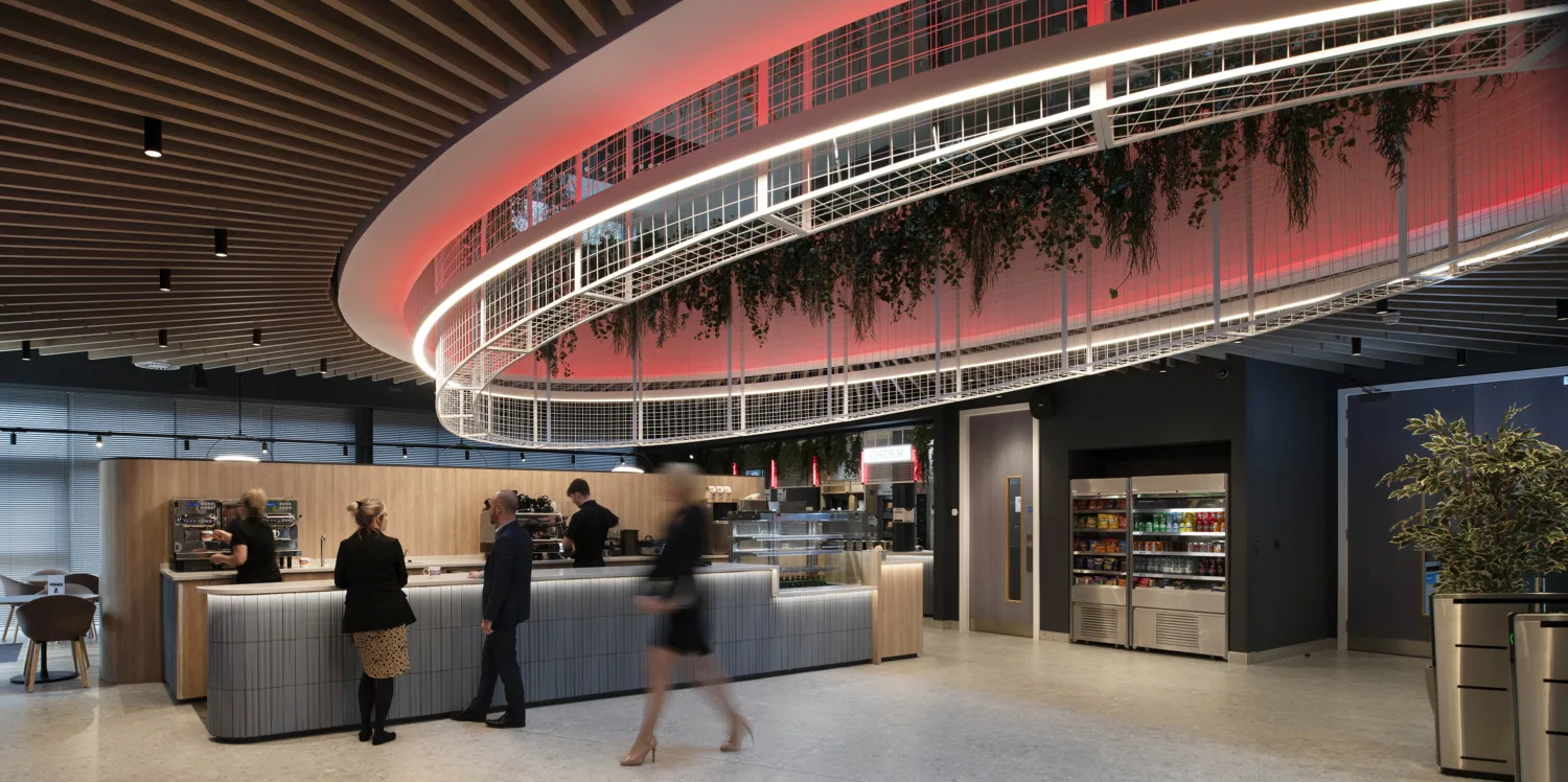 Modern office reception with greenery and plants coming from the light fixtures in the ceiling, and people chatting and walking