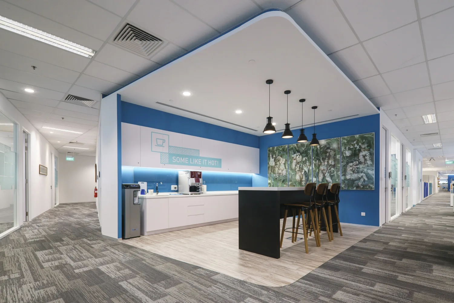 Open pantry space featuring water cooler, coffee machine, a long table with chairs and overhanging lights, and quadriptych wall decor