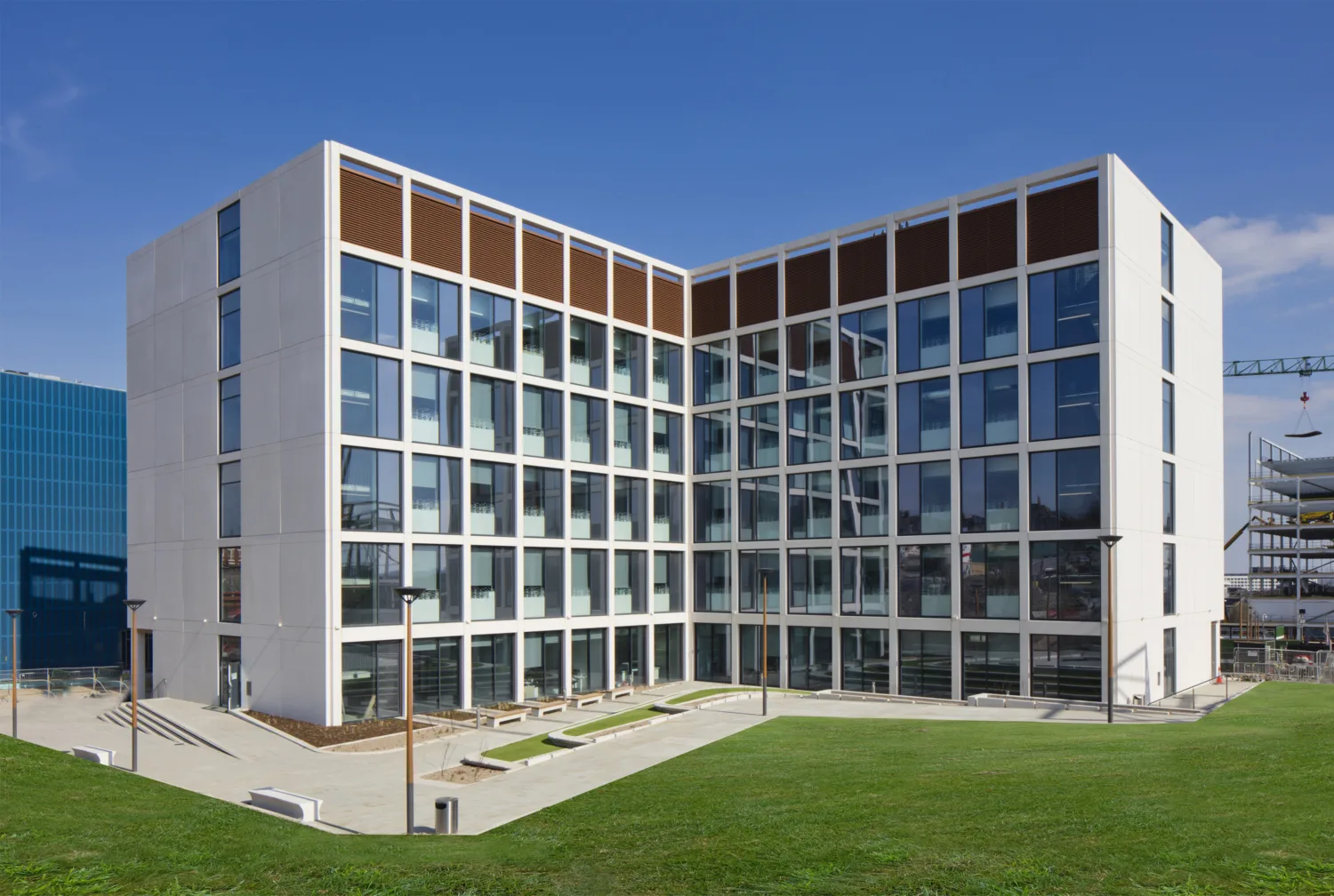 The exterior of a white walled building with regular square windows, in front of which is a grassy verge, all against a blue sky