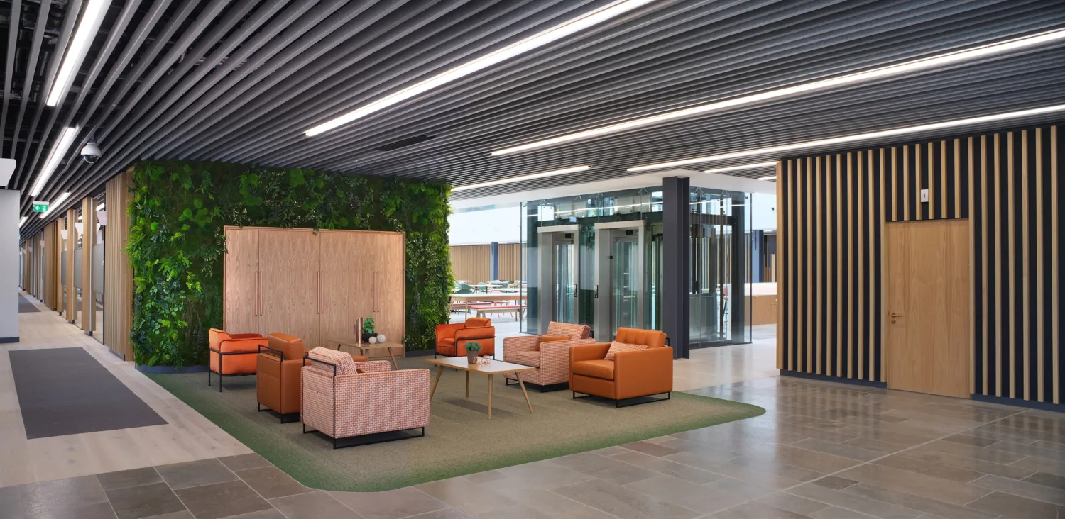 Reception area, sofas and coffee table in centre, green wall behind, lift shaft far right