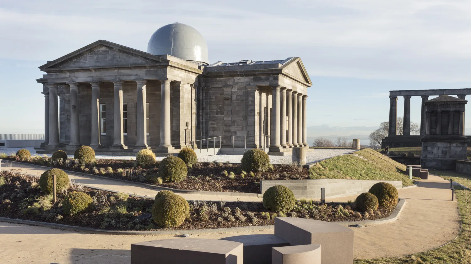 Central building with stone pillars and a dome on the roof with walkways in the foreground