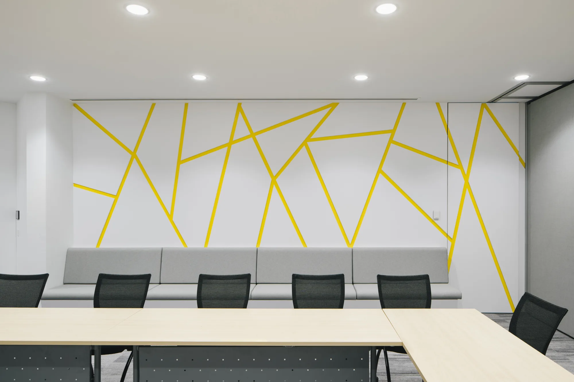 Open meeting space featuring L-shaped table lined with office chairs and a couch along the back wall with a geometric wallpaper