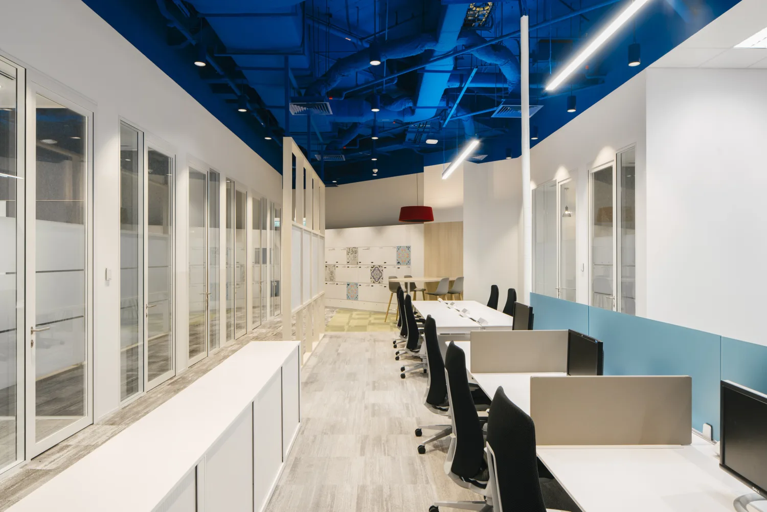 Carpeted workspace featuring single row of individual desks each with a desk chair and computer