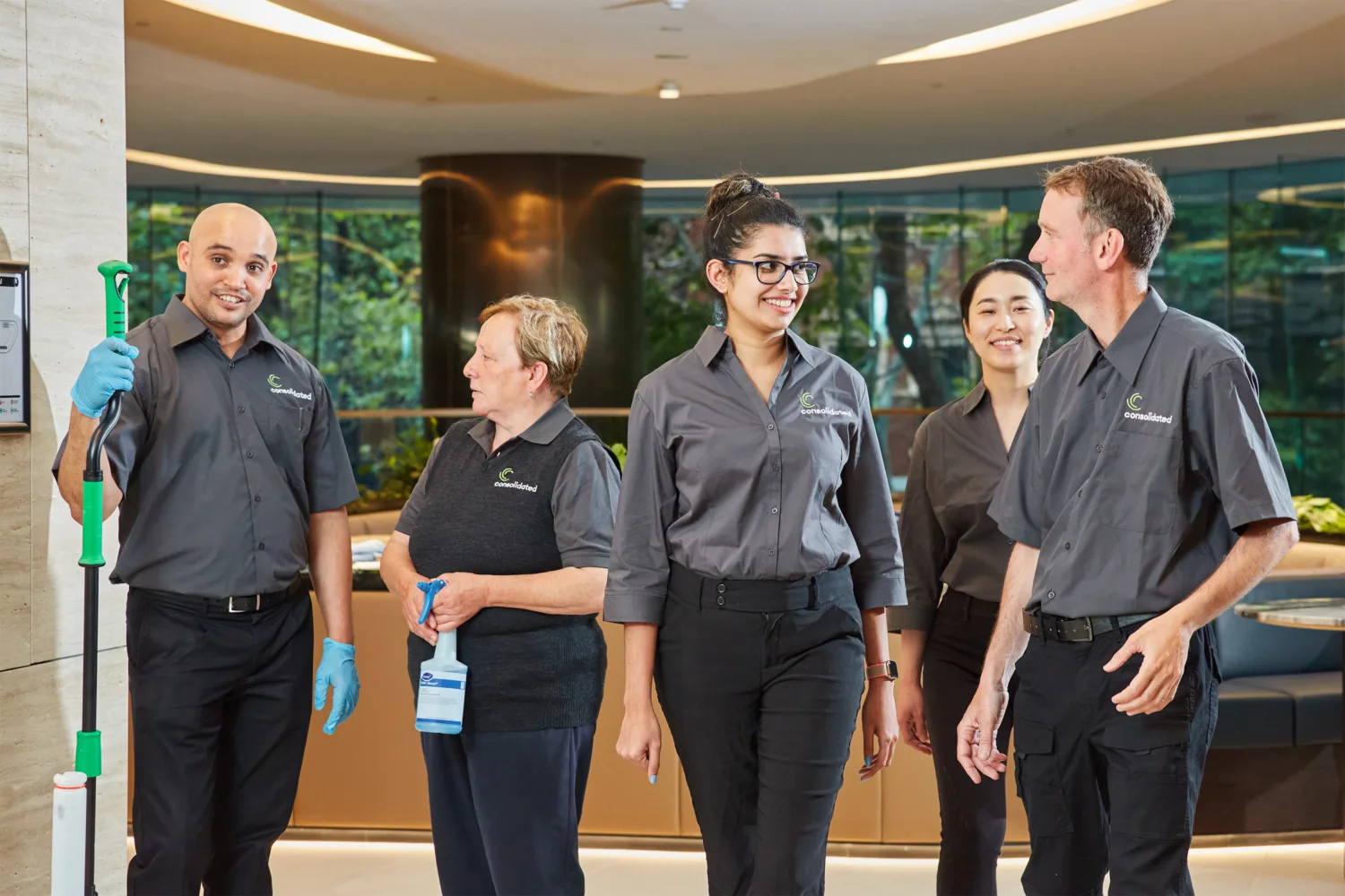 group of 2 men and 3 women standing in an entrance lobby dressed in CPS uniforms hoding cleaning products