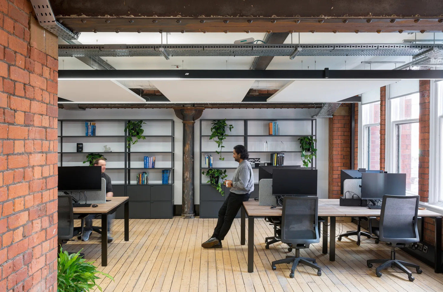 Open plan office with wooden floors and exposed brickwork walls, with two employees in conversation