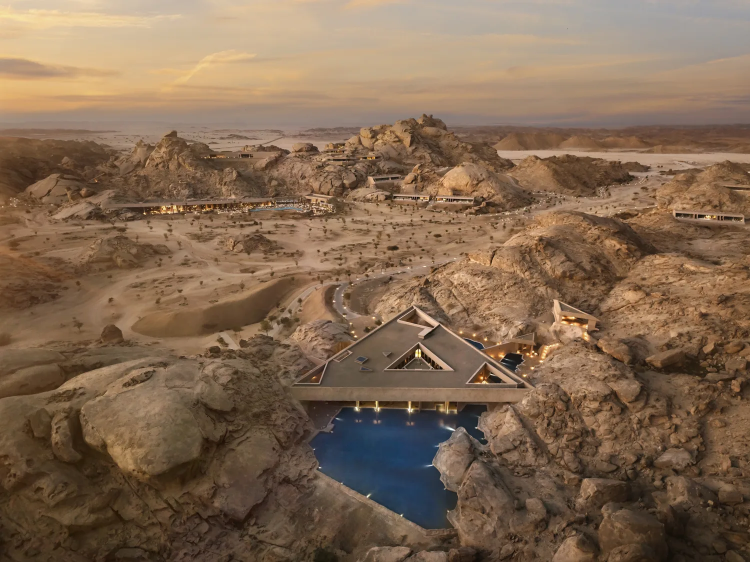 Aerial view of buildings integrated into a rocky desert landscape, with pools, pathways and surrounding rock formations.