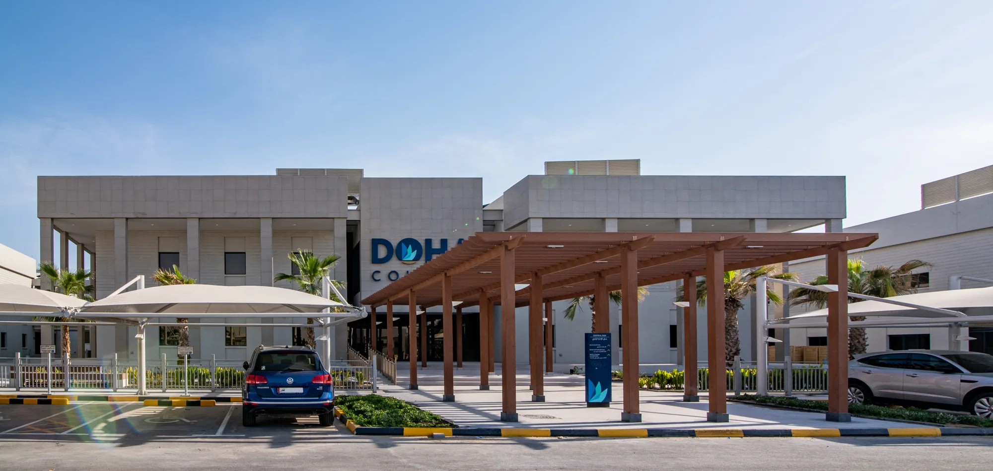 Entrance of Doha College with wooden roof terrace, wayfinder and parking area