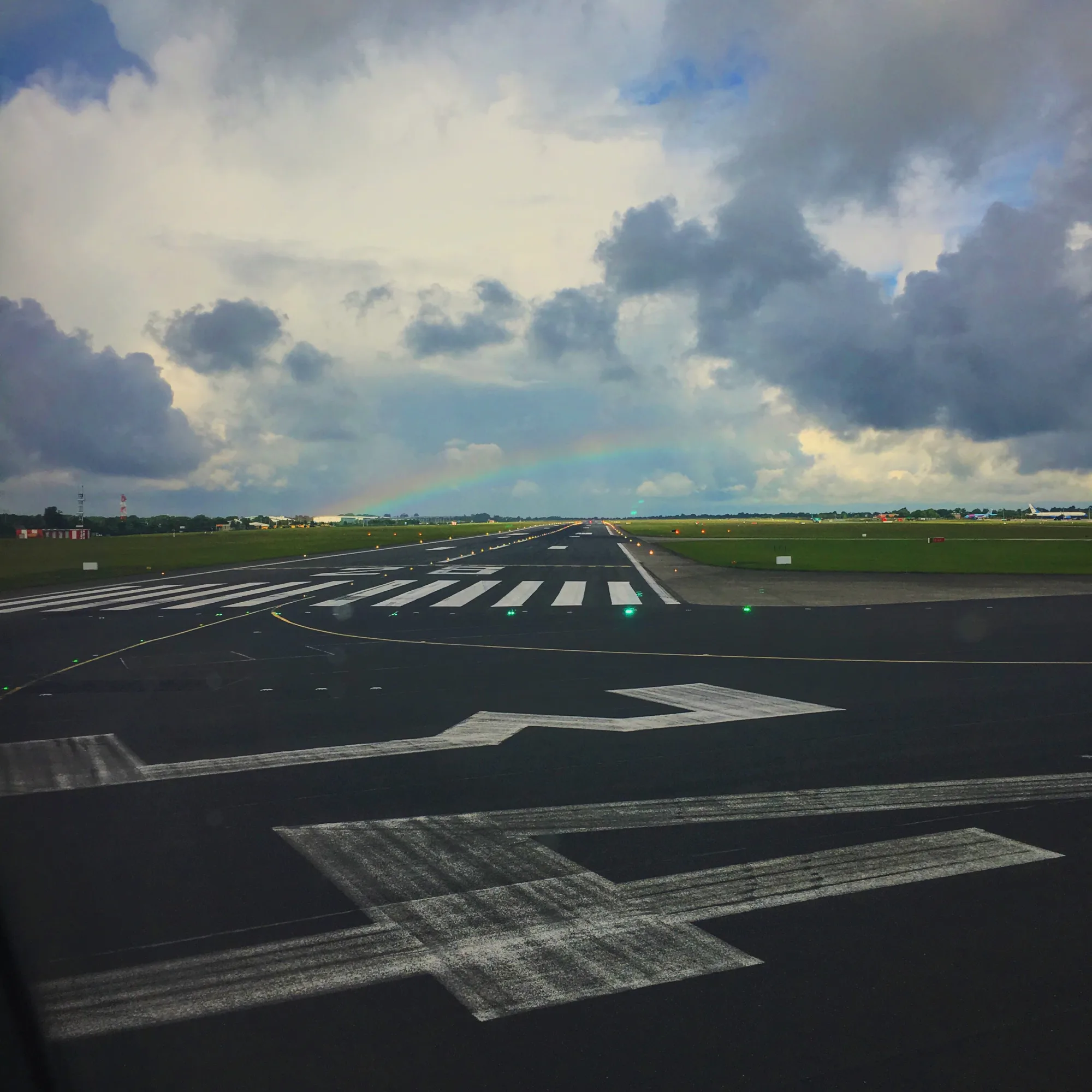 Airport runway under a grey cloudy sky and a faint rainbow