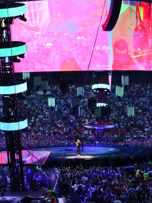 Ed Sheeran on stage at night with lighting on podiums and fans surround the stage