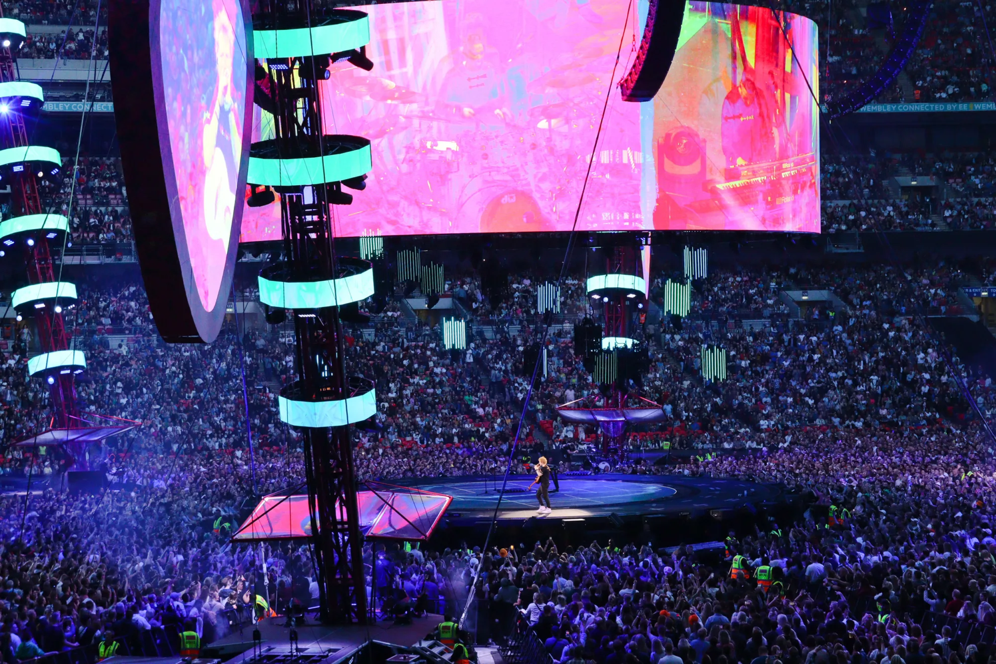 Ed Sheeran on stage at night with lighting on podiums and fans surround the stage