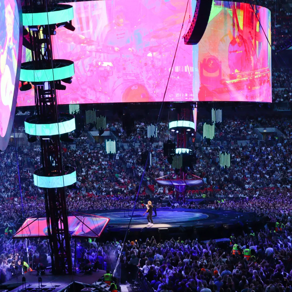 Ed Sheeran on stage at night with lighting on podiums and fans surround the stage