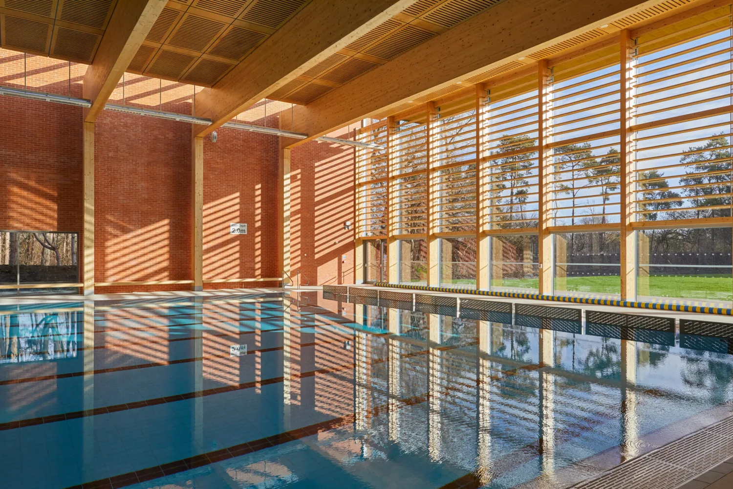 Large indoor swimming pool with a wooden roof overhead and full-length windows at end of pool.