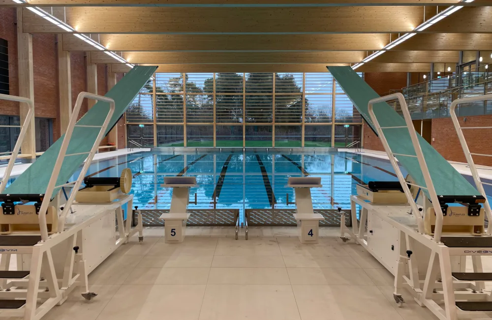 Swimming pool with diving boards, wooden roof overhead, full-length windows at end of pool