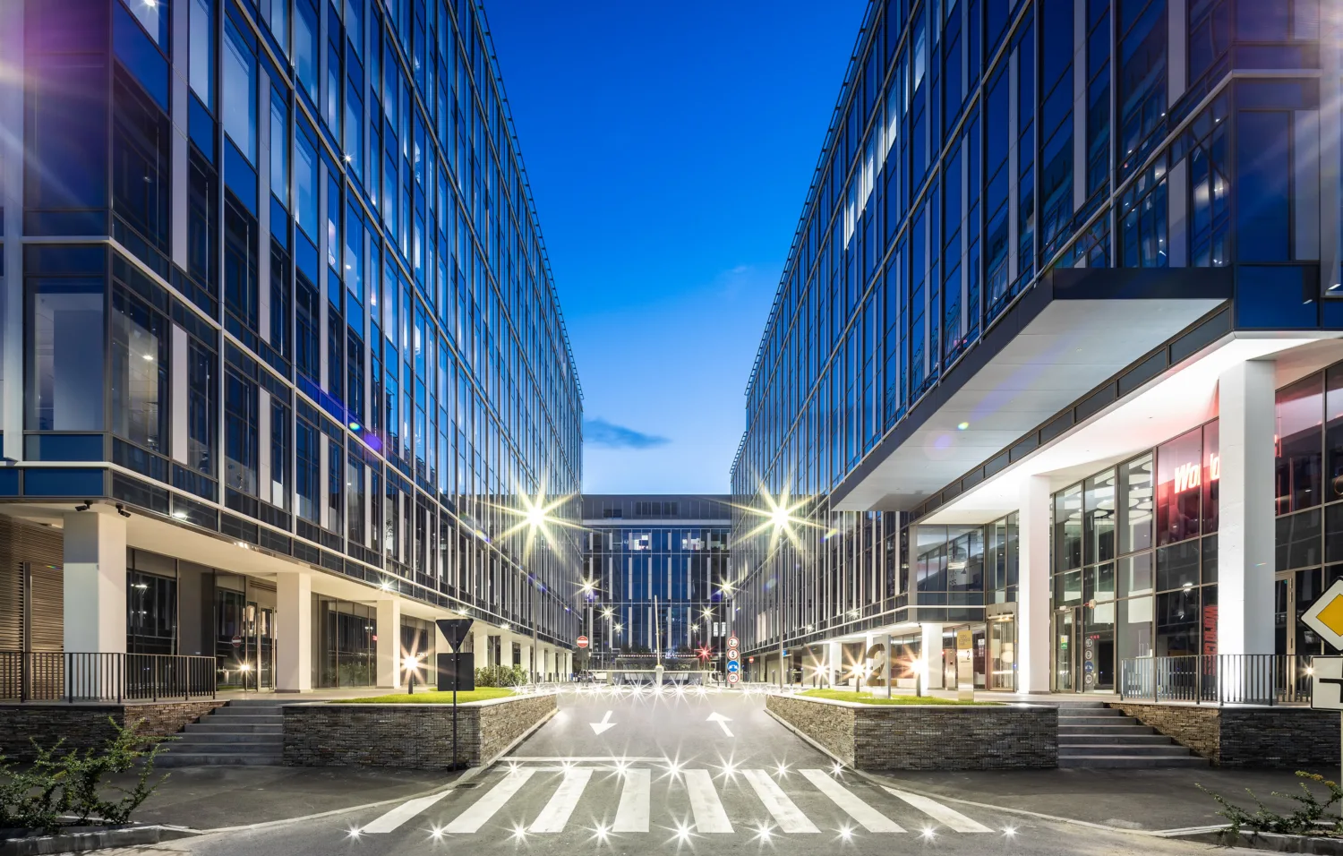Road with zebra crossing leading between 2 glazed buildings at dusk