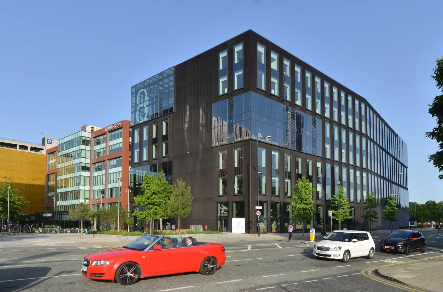 Exterior large dark grey building next to a street with several cars