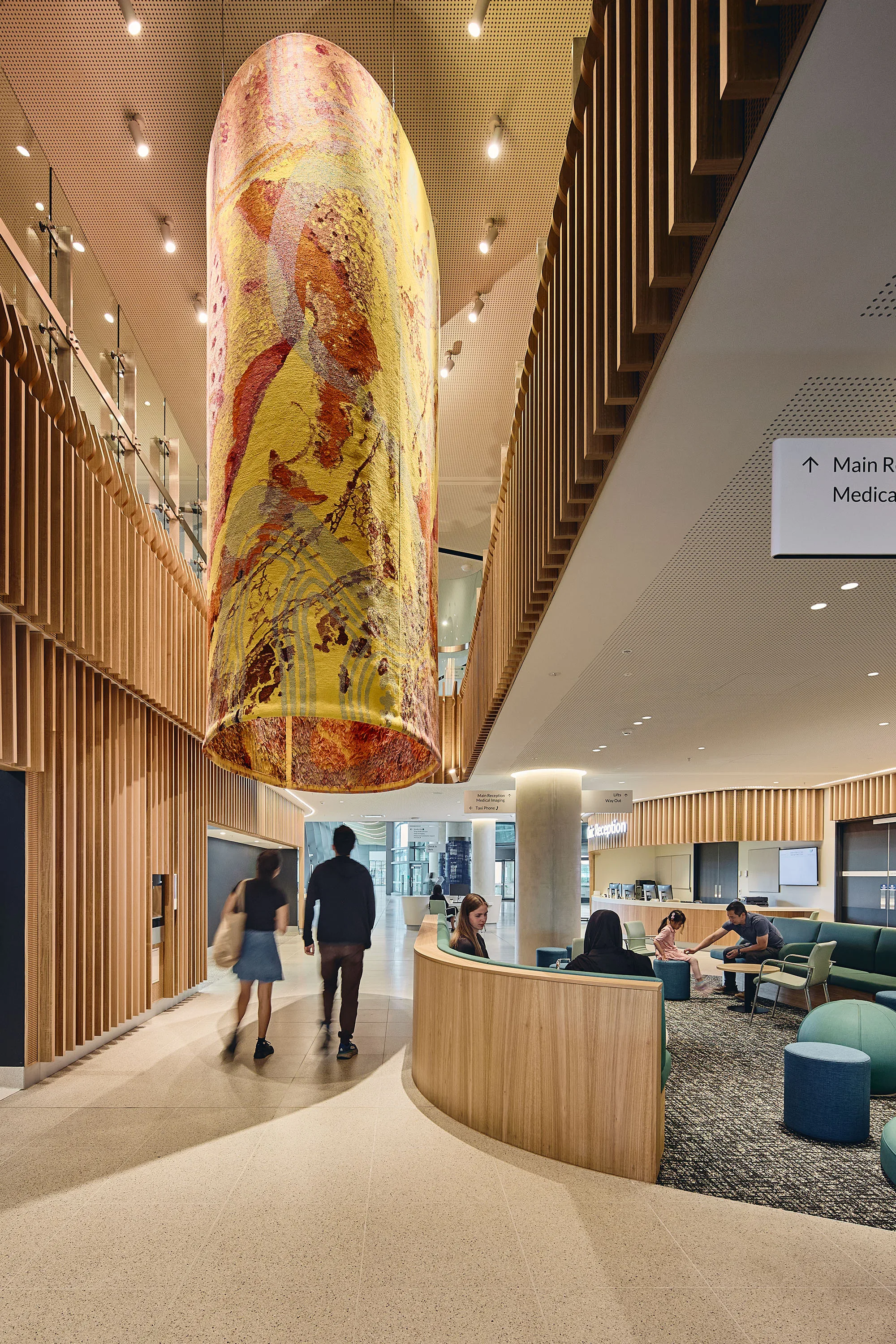 Interior reception area with curved timber-lined walls, seating, overhead lighting and a suspended cylindrical textile artwork.