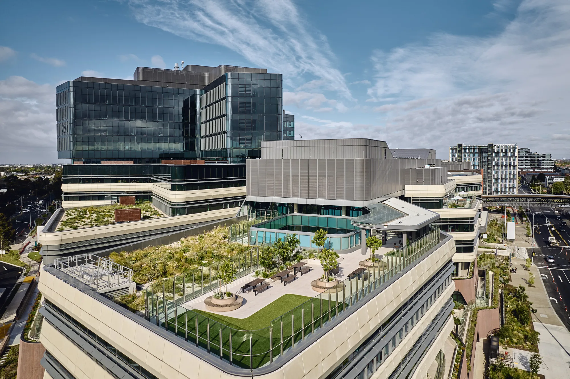 Elevated terrace with landscaped planting, seating areas, glass balustrades and surrounding views of a multi-storey healthcare building.