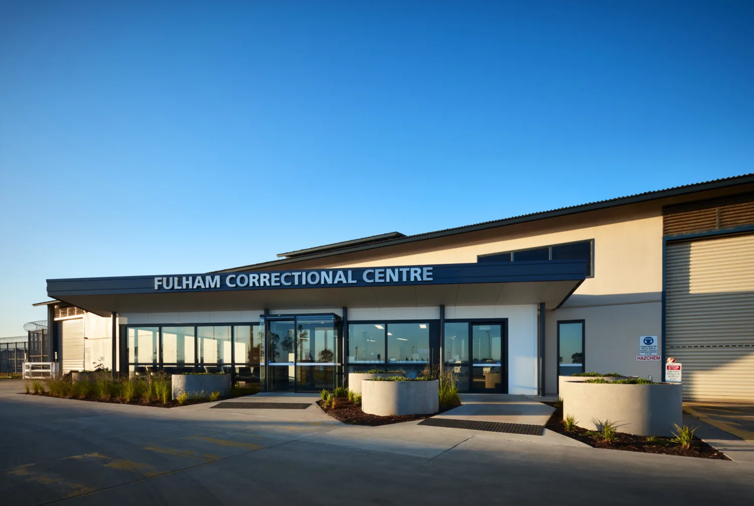 Exterior view of main entrance to Fulham Correction Facility with sign above front doors and blue sky behind.