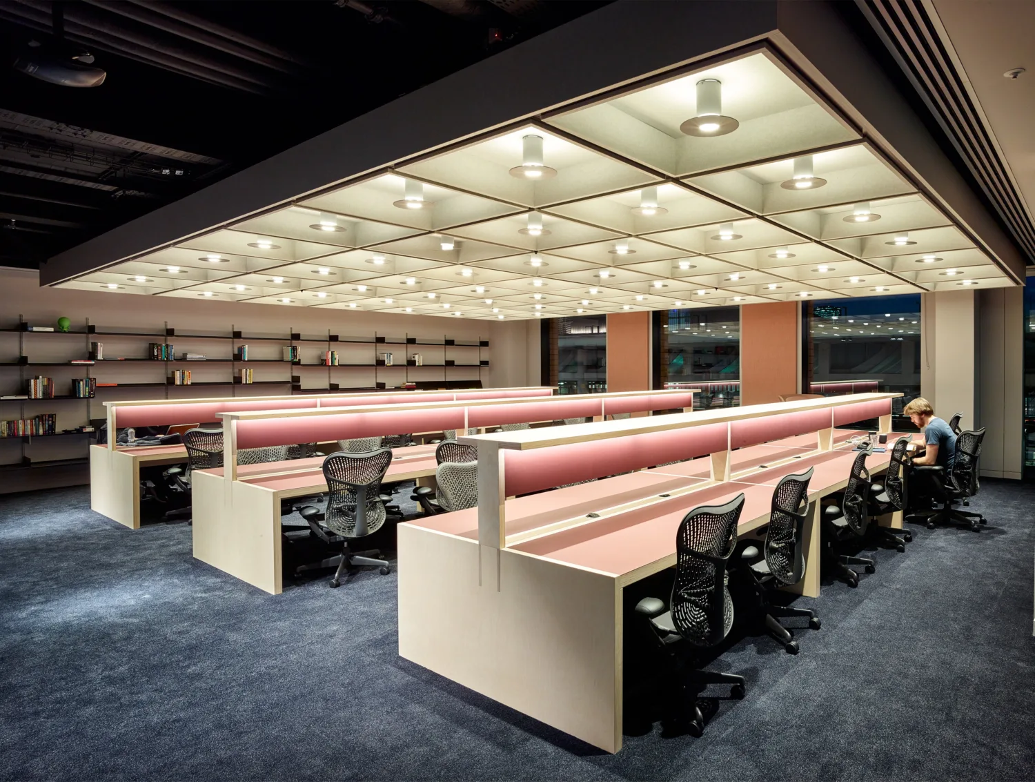 Interior rows of brightly lit desks with accompanying desk chairs, one of which someone is sitting in