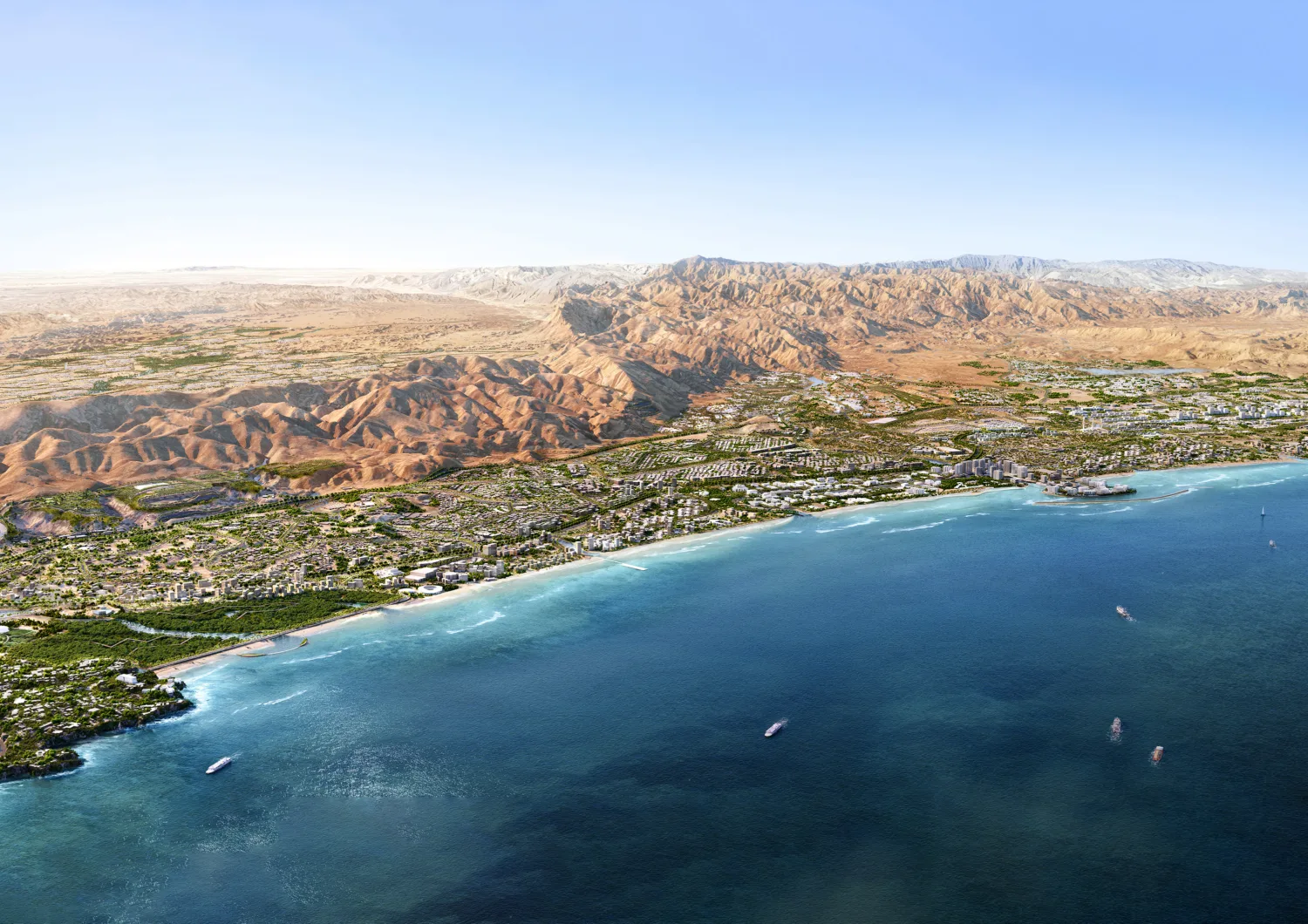 Aerial view of a coastal city with dense greenery, buildings, and roads along a curved shoreline. Clear blue water fills the foreground, and a wide expanse of rocky, beige mountains stretches across the background.