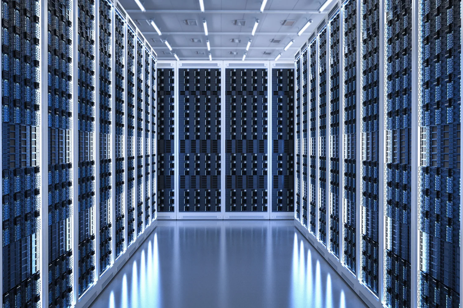 A symmetrical aisle inside a data center with tall server racks on both sides, filled with cables and hardware components, illuminated by bright white ceiling lights.