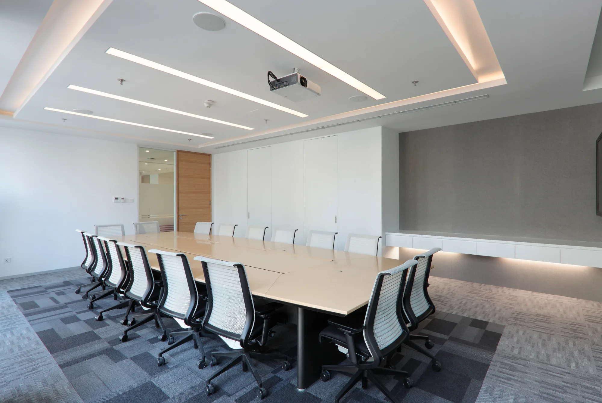 Carpeted meeting room featuring overhead projector and long conference table lined with office chairs