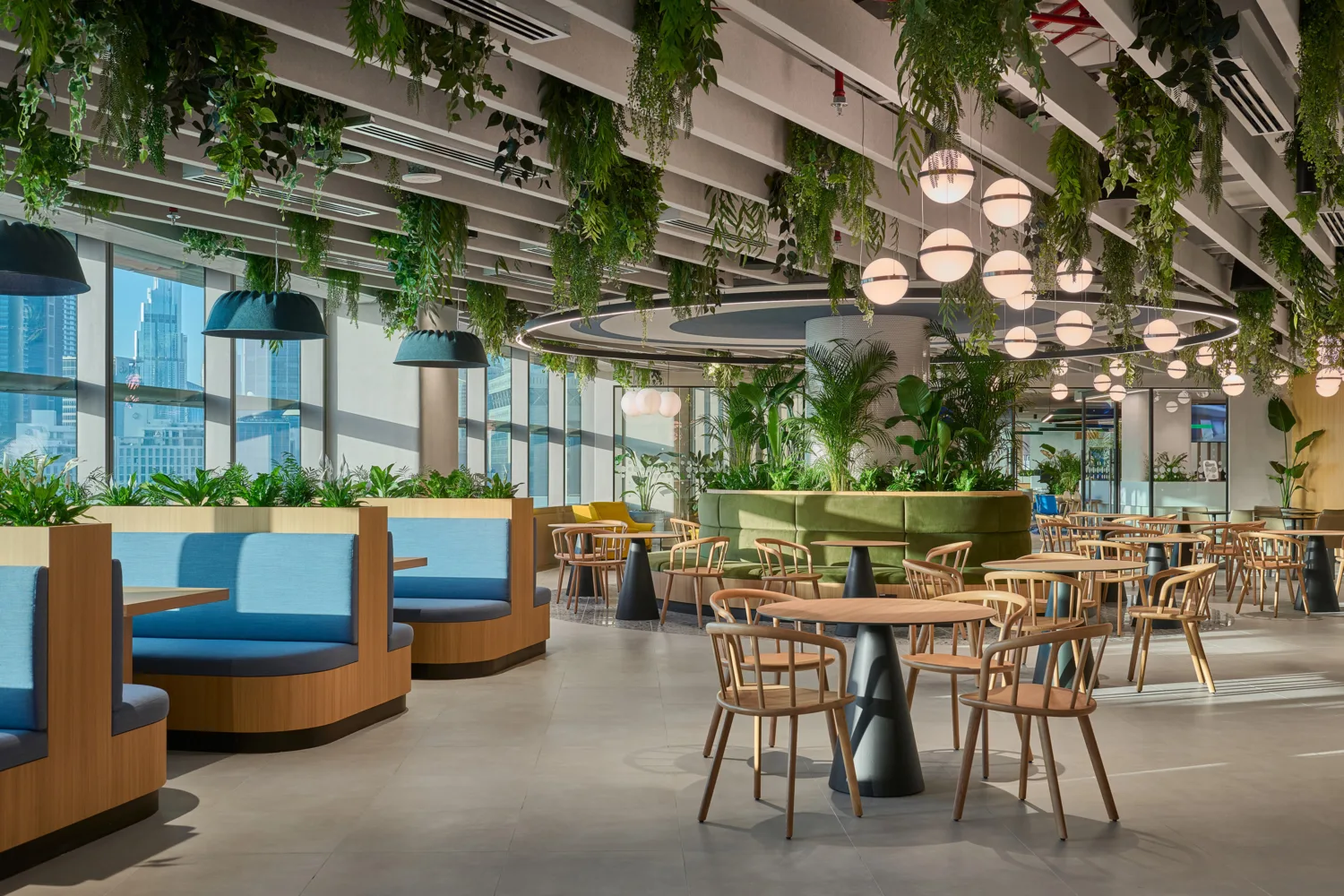 Informa office seating area with wooden table and chairs and blue booths with green plants as decoration and the Dubai skyline in the distance.