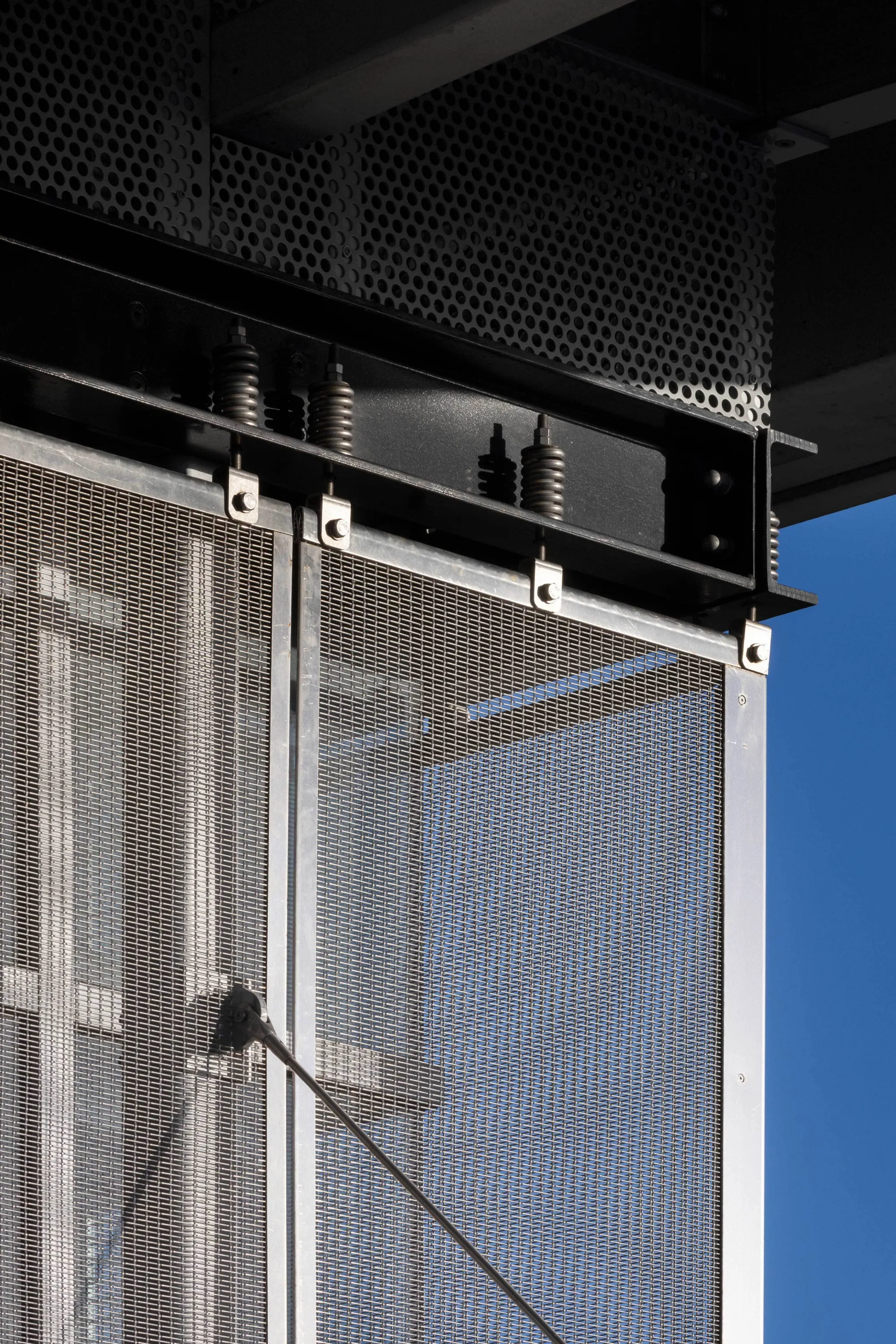 Close-up of metal mesh panels of Kishoge station building façade against a clear blue sky