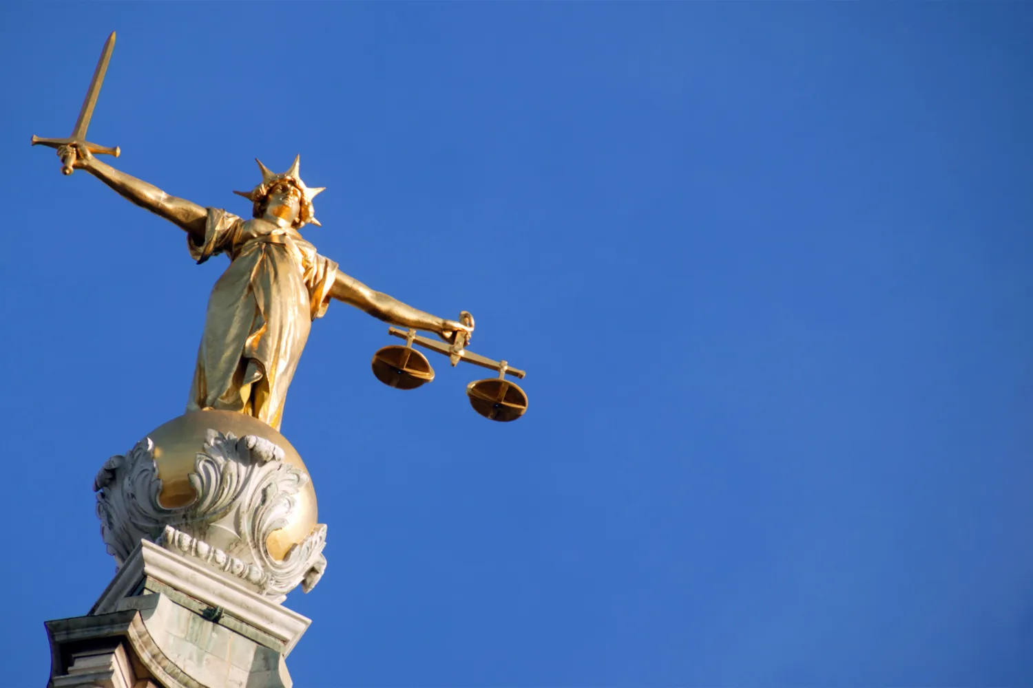Statue in gold of lady justice holding a swod and set of scale against a blue sky