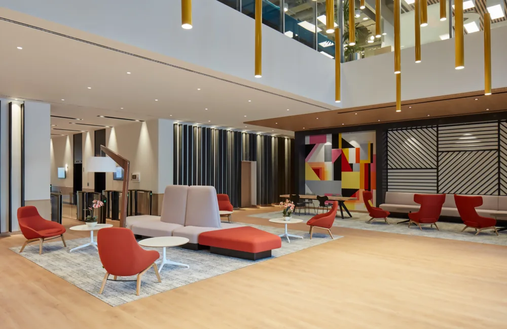 PWC Middle East large guest and meeting area with ample amount of desks and chairs while being illuminated by artistic chandeliers. A smart, secure and modern bio metrics entrance is also visible.