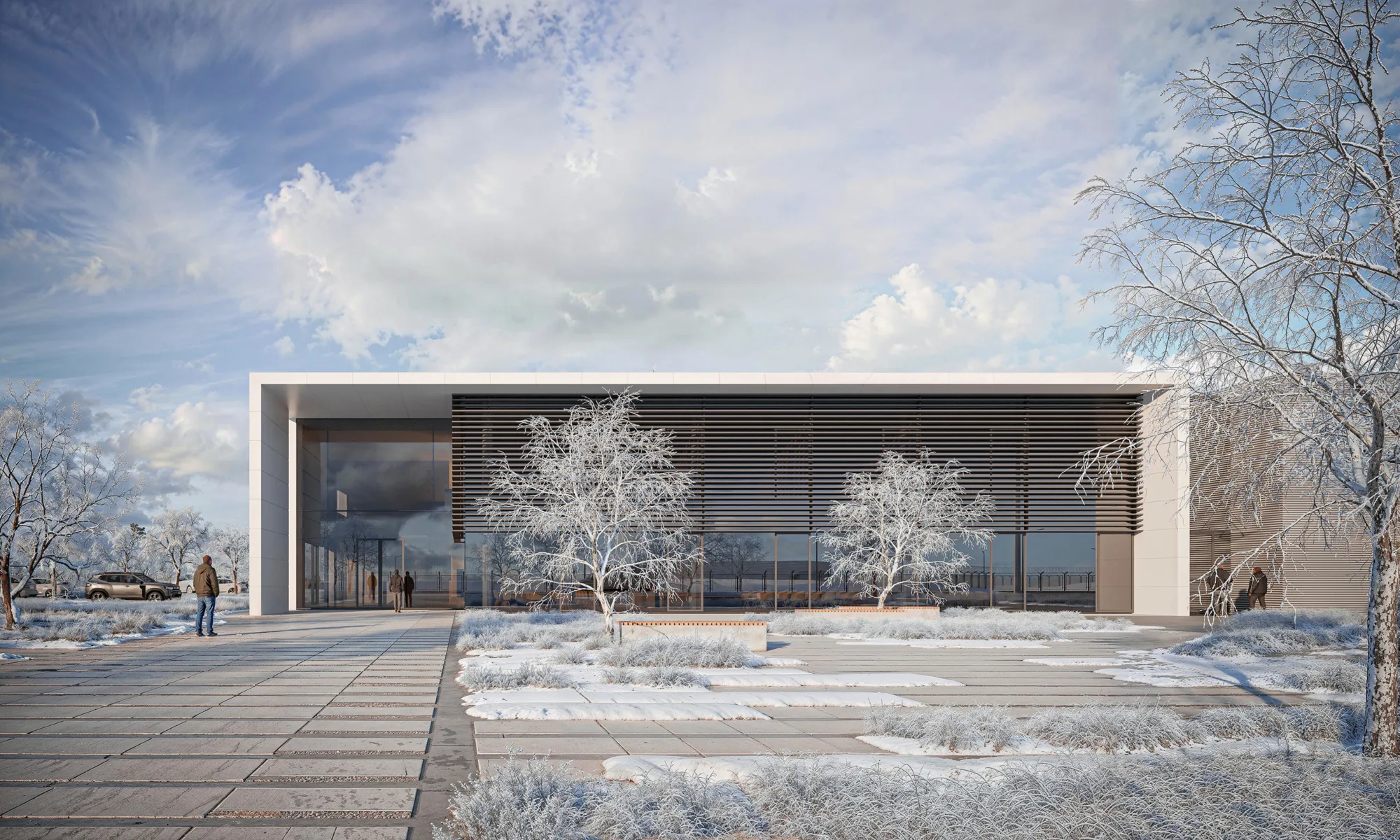 Modern building entrance in a winter setting, featuring a large glass façade, horizontal sunshades, and frost-covered trees and landscaping. Several small human figures stand near the entrance and walkway, with a parked vehicle visible to the left. Cloud-filled sky overhead. No visible text.