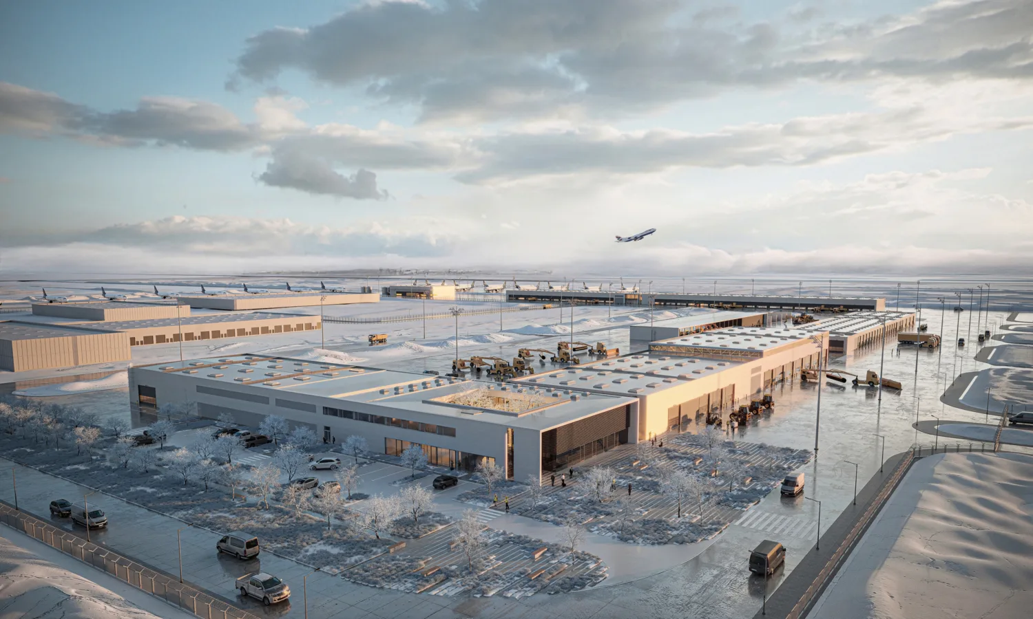 Aerial view of a large airport support campus in a snowy landscape. Several industrial buildings, parking areas, service vehicles, and light poles are visible. Multiple aircraft are parked in the distance, and one aircraft is airborne above the horizon. Snow-covered roads and landscaped areas surround the site. No visible text.