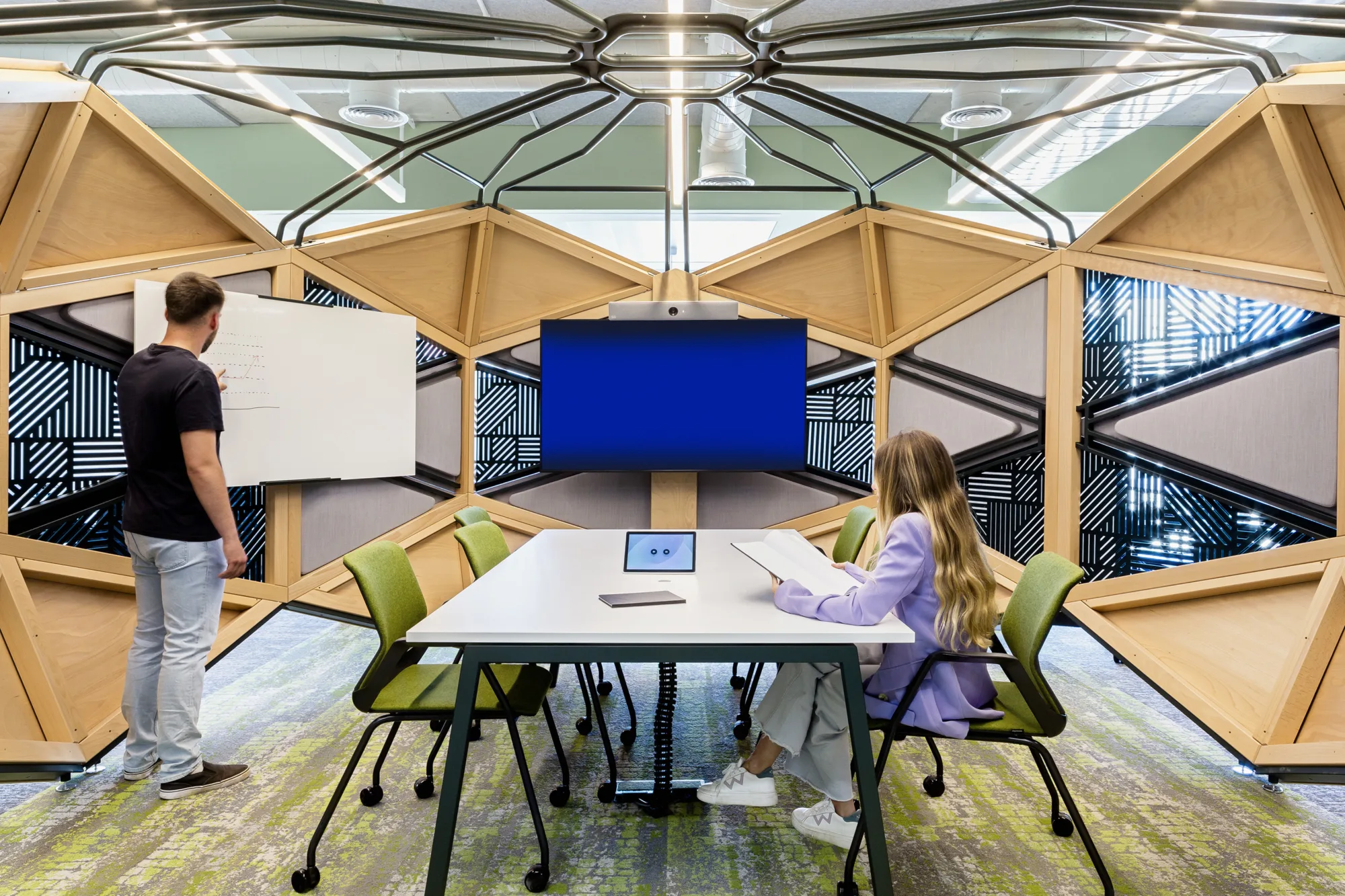 Breakout collaboration spaces with wooden panelling, a large desk and screens on the wall.