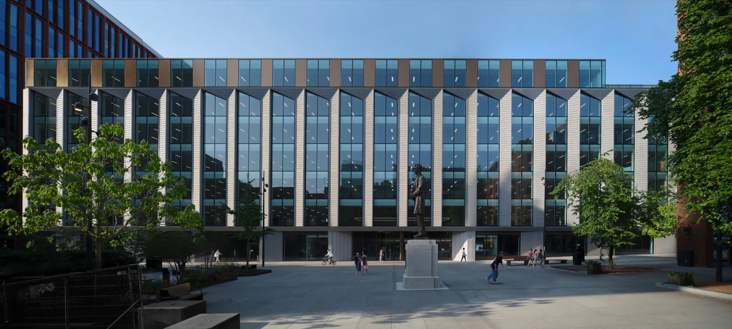 Landscape shot of the exterior of the building with a statue in front and people walking in the foreground