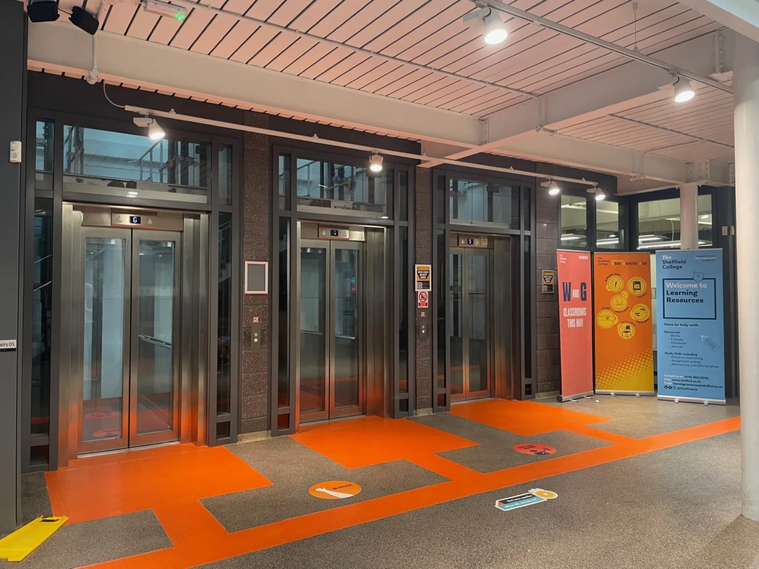 Three glass lift doors with red textured flooring at the entrance