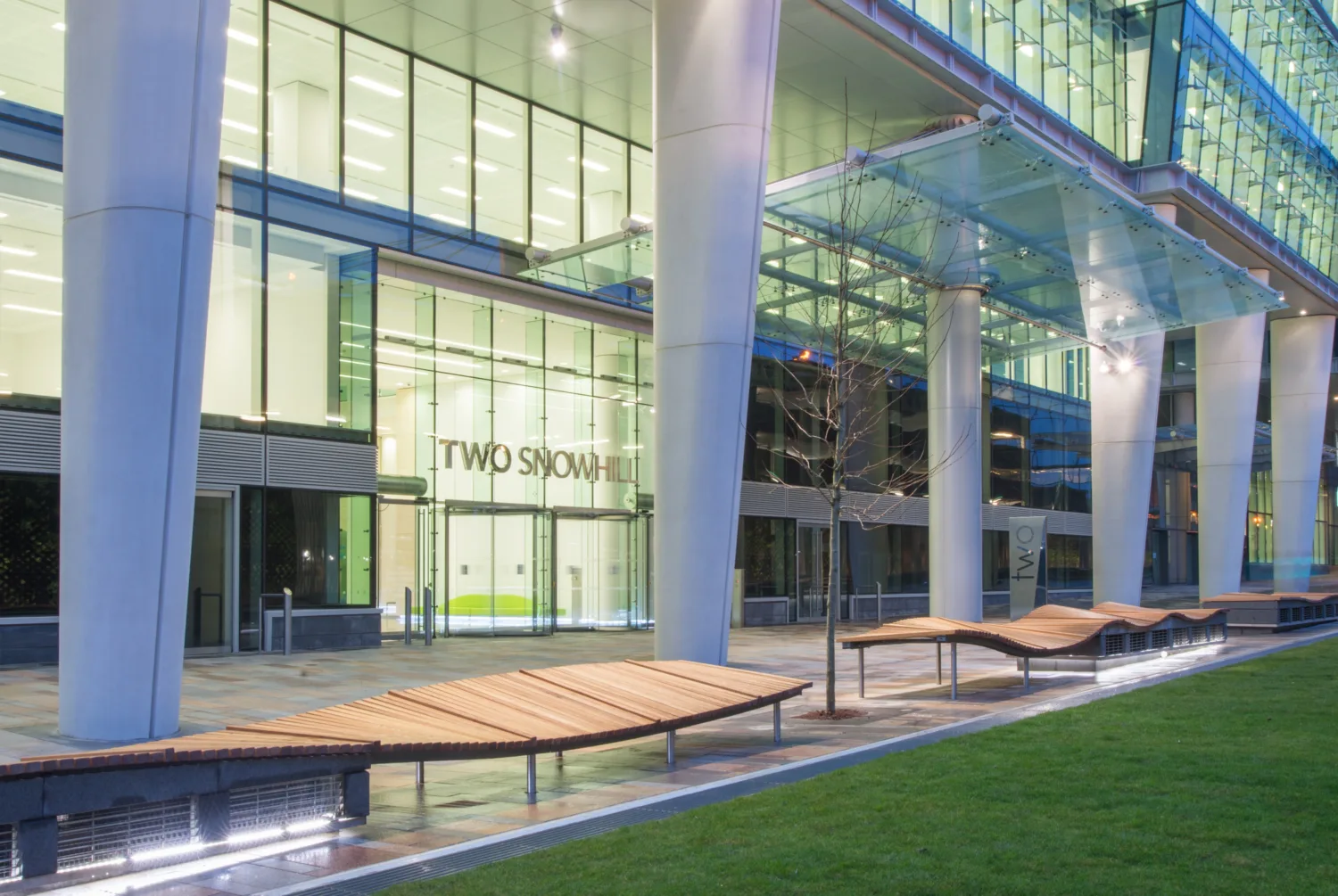 Exterior lobby of Two Snowhill lit from inside with several white supporting pillars visible